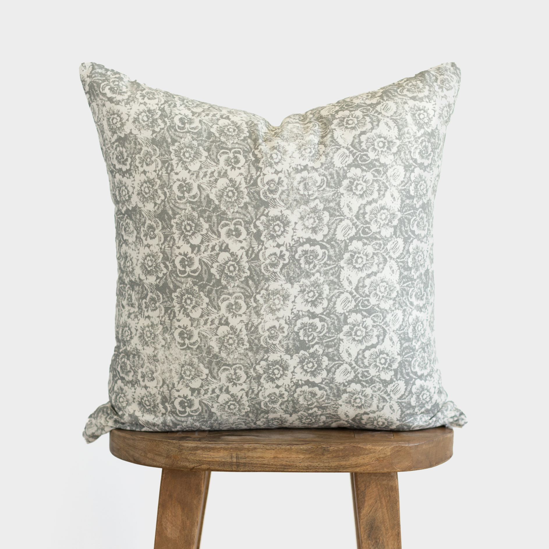 Gray and white damask floral patterned pillow cover on wooden stool.