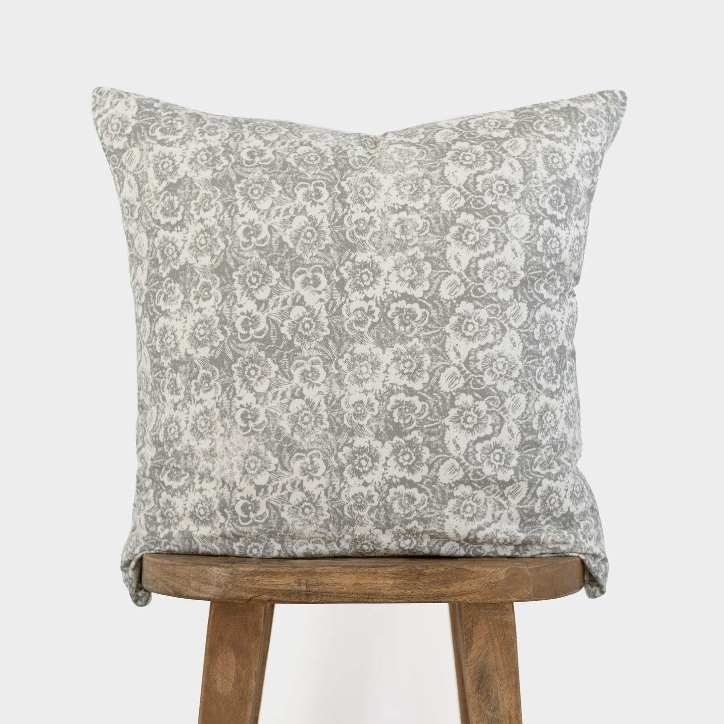 Gray and white floral patterned throw pillow displayed on wooden stool legs.
