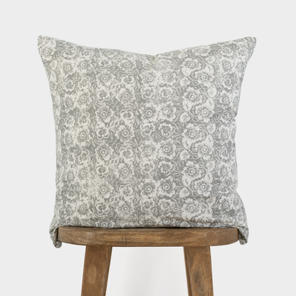 Gray and white floral patterned throw pillow displayed on wooden stool legs.