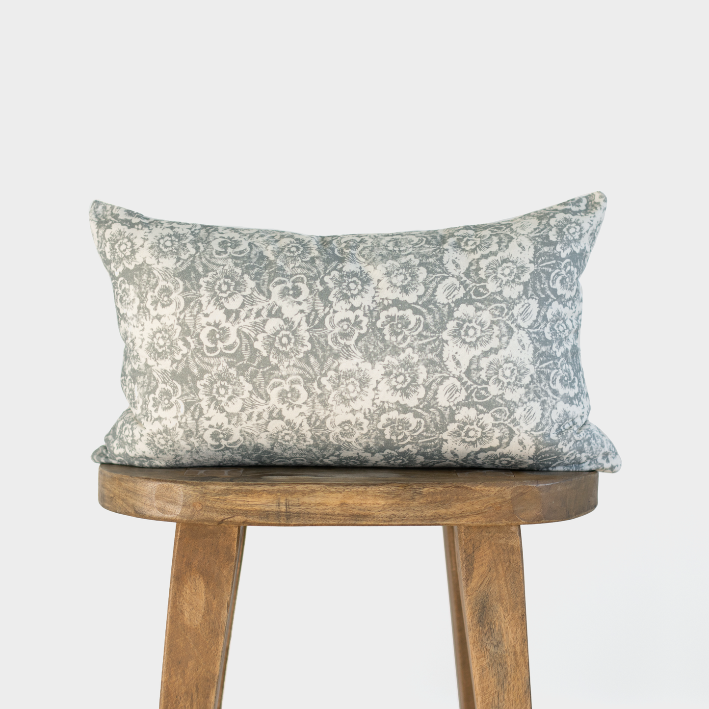 Gray and cream floral patterned lumbar pillow displayed on a wooden stool.
