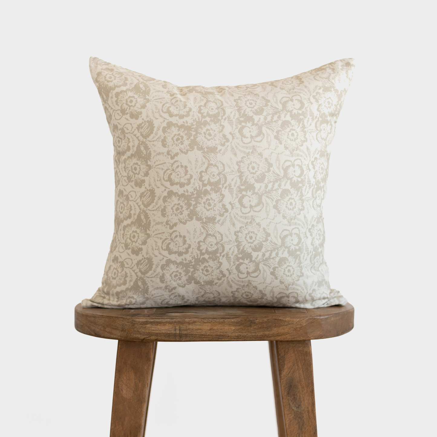 Cream pillow cover with beige damask floral pattern, displayed on wooden stool.