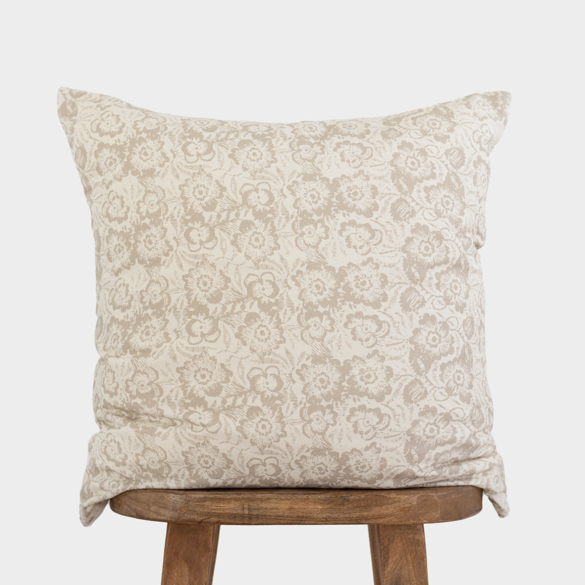 Beige pillow cover with damask floral pattern in neutral tones, displayed on wooden stool.