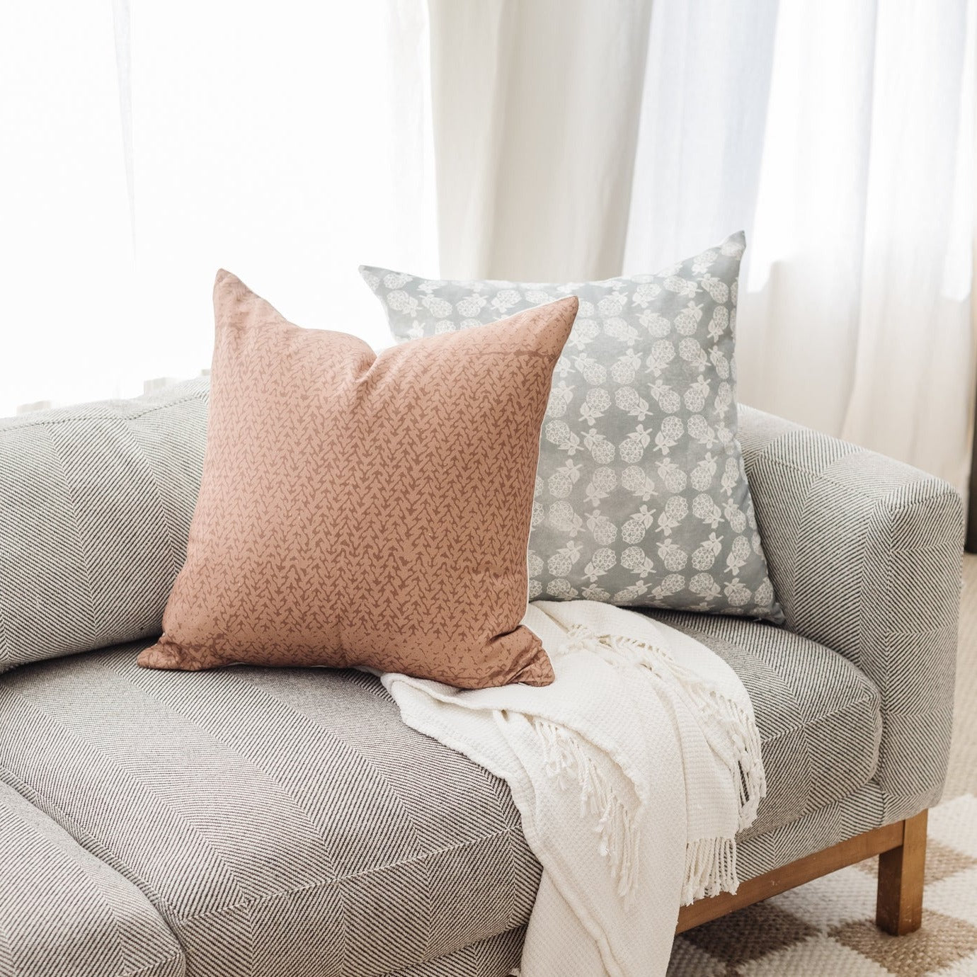 Pink textured pillow and gray floral pillow displayed on a beige striped sofa.