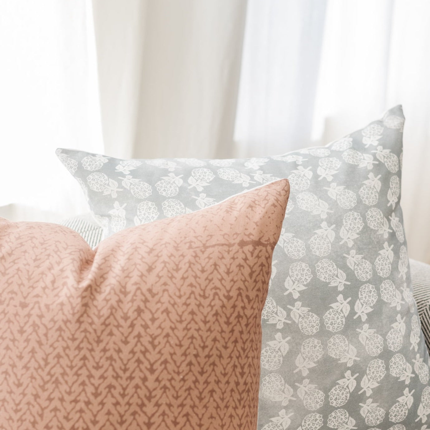 Pink textured pillow next to gray pillow with white floral pattern, both displayed on a bed with white bedding.