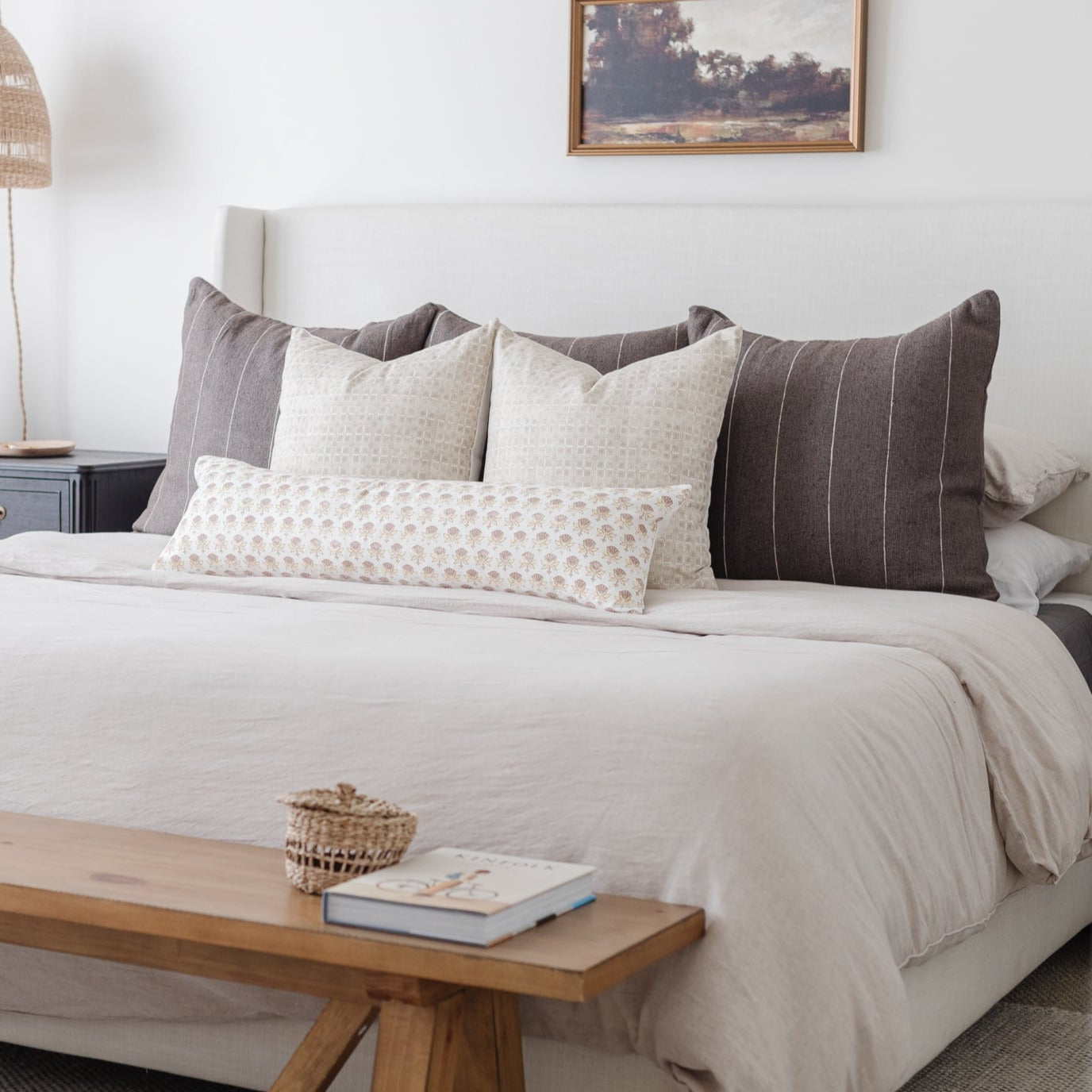 Bed styled with five decorative pillows in cream and charcoal tones with grid and textured patterns.