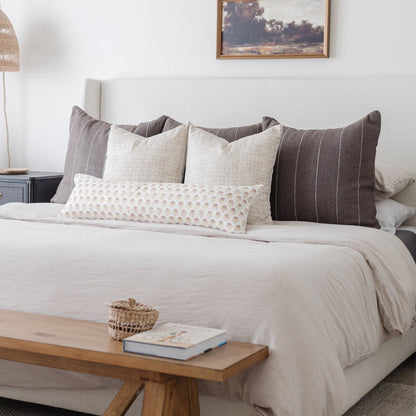 Bed styled with five decorative pillows in cream and charcoal tones with grid and textured patterns.