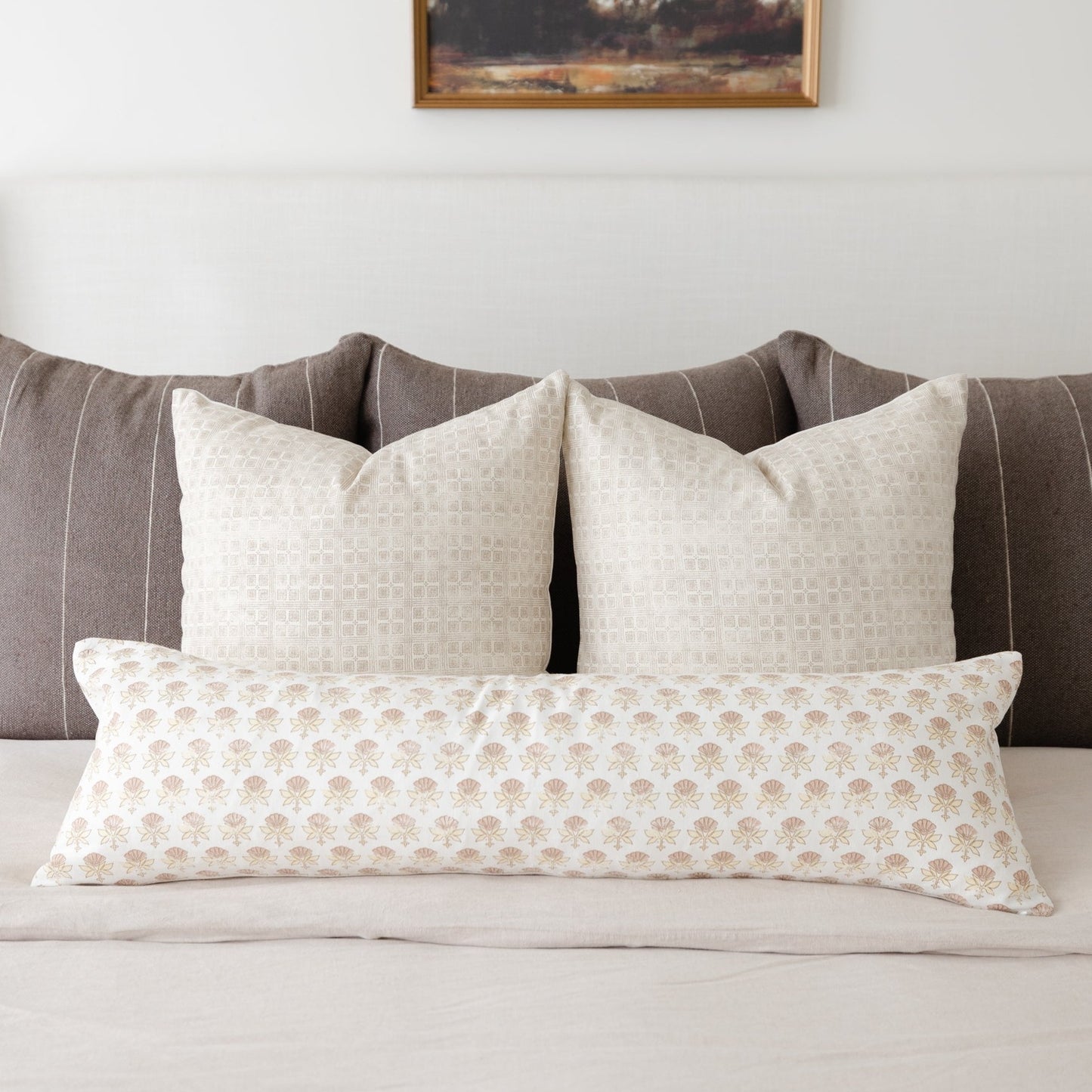 Three cream and tan patterned throw pillows arranged on a gray striped upholstered bed headboard.