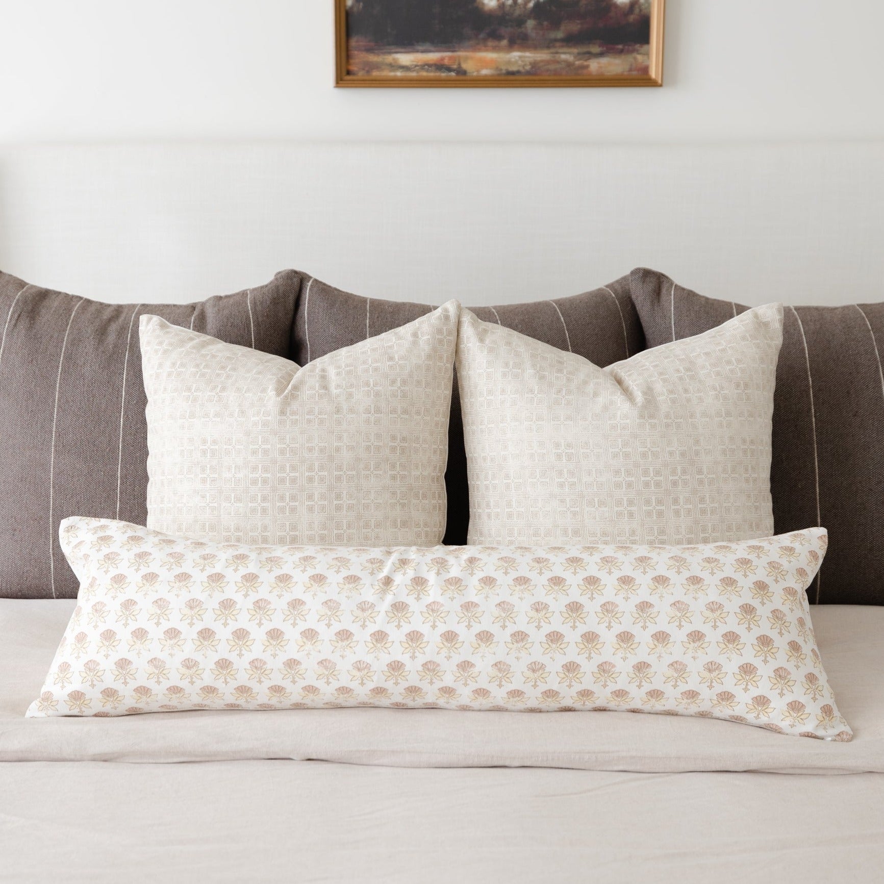 Three cream and tan patterned throw pillows arranged on a gray striped upholstered bed headboard.