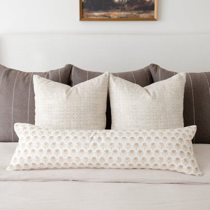 Three cream and tan patterned throw pillows arranged on a gray striped upholstered bed headboard.