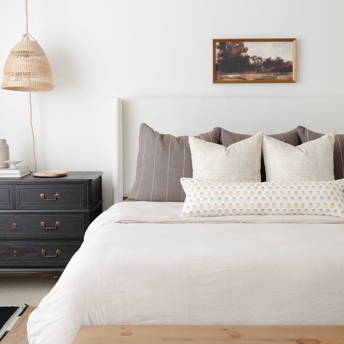 Bed with white duvet, cream and taupe patterned pillows, and gray upholstered headboard in bedroom setting.