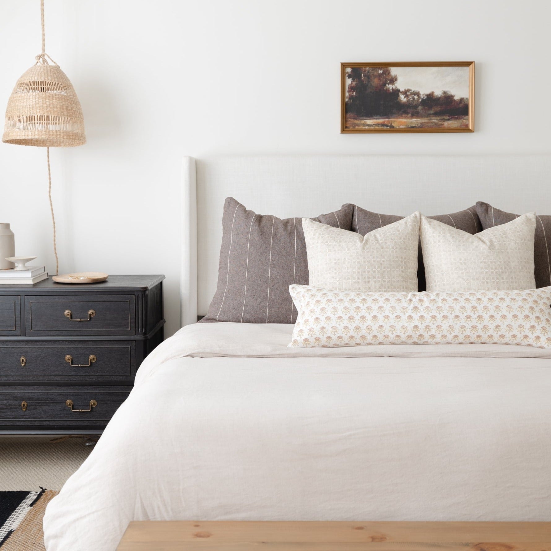 Bed with white duvet, cream and taupe patterned pillows, and gray upholstered headboard in bedroom setting.