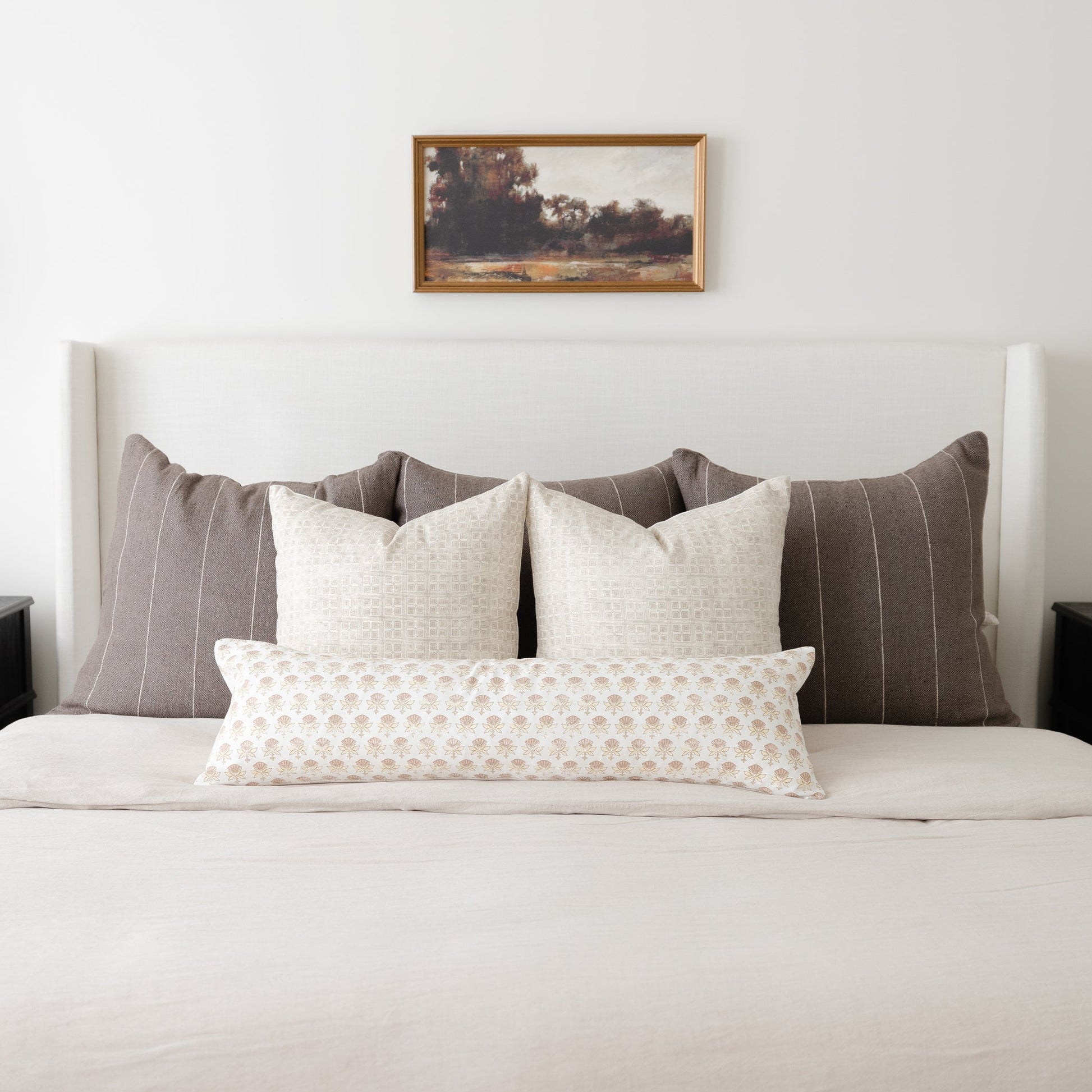 White lumbar pillow with beige floral pattern displayed on bed with striped and solid pillows.