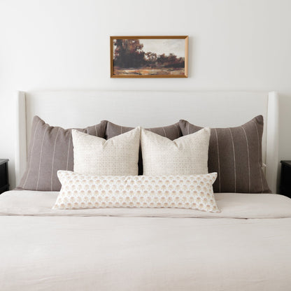White lumbar pillow with beige floral pattern displayed on bed with striped and solid pillows.