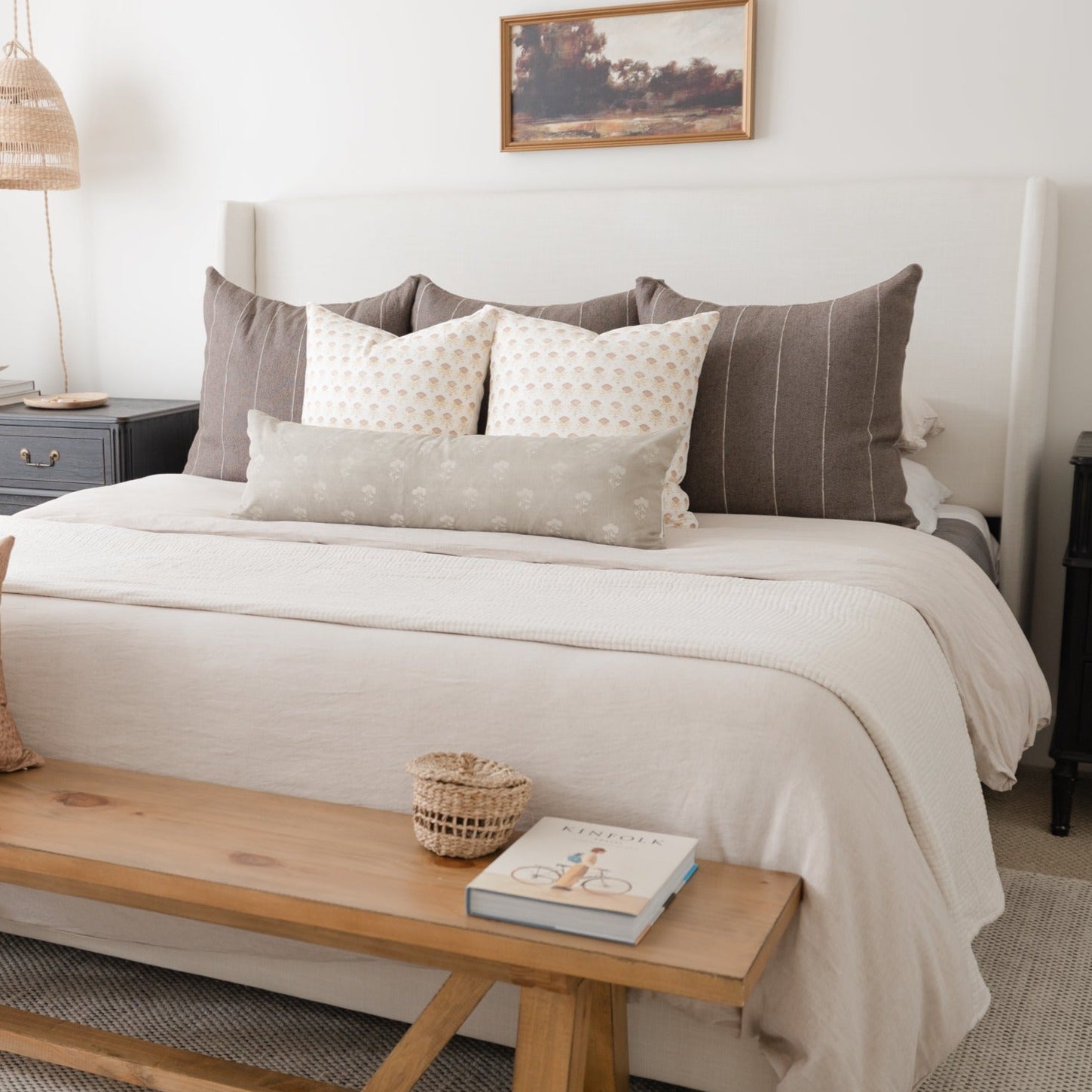 White rectangular lumbar pillow with small floral pattern displayed on bed with gray and cream pillows.