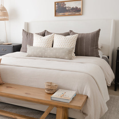 White rectangular lumbar pillow with small floral pattern displayed on bed with gray and cream pillows.