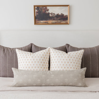 White floral patterned decorative pillows arranged on a gray upholstered bed headboard.