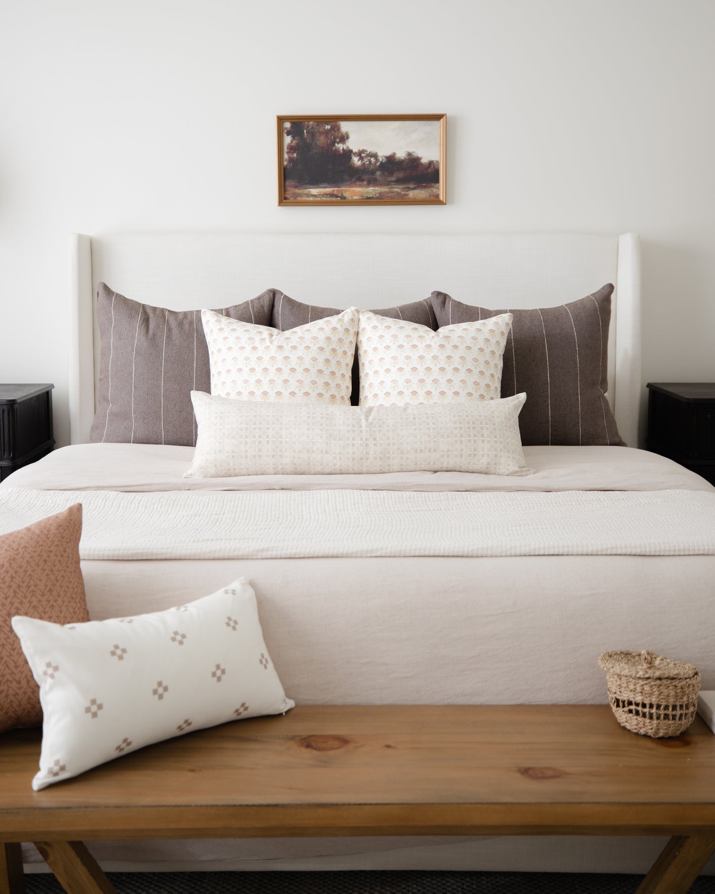 Cream lumbar pillow with small geometric floral pattern displayed on wooden bench in front of bed.