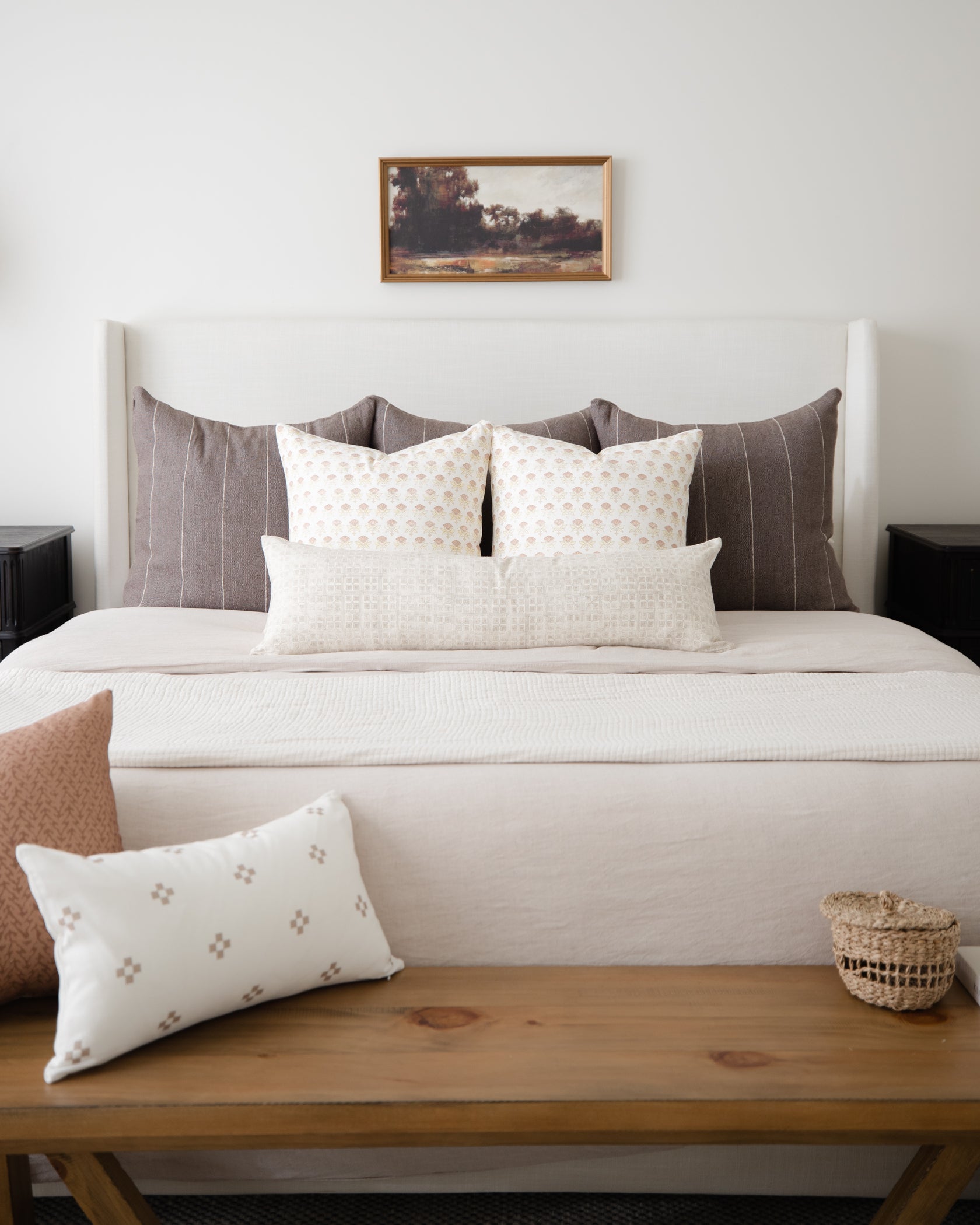 Cream lumbar pillow with small geometric floral pattern displayed on wooden bench in front of bed.