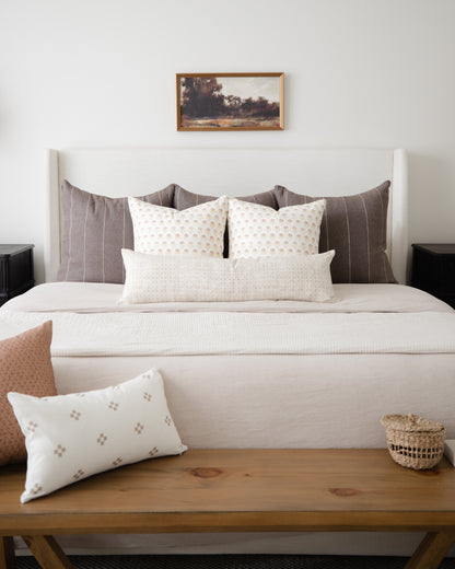 Cream lumbar pillow with small geometric floral pattern displayed on wooden bench in front of bed.