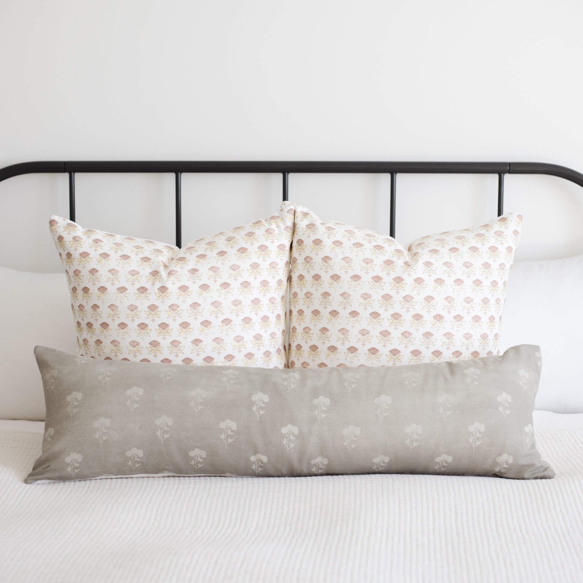 Gray lumbar pillow with white floral pattern displayed on bed with coordinating patterned pillows.