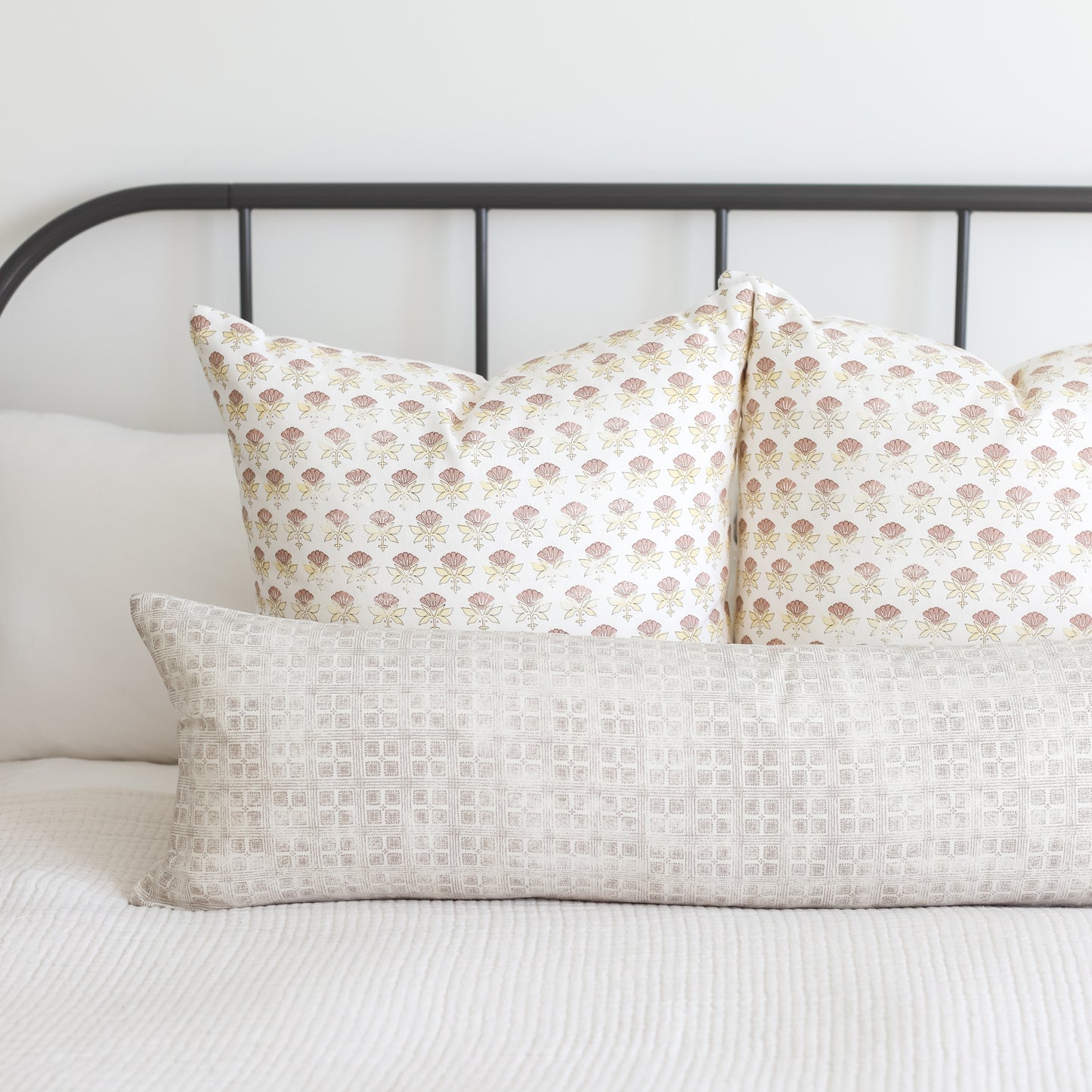 Rectangular lumbar pillow with light beige grid pattern displayed on bed with coordinating floral pillows.