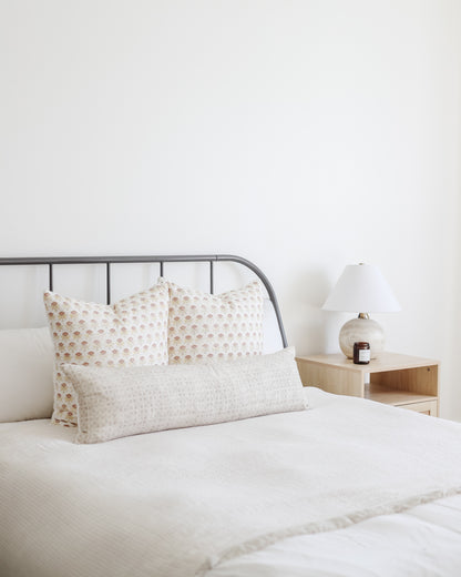 Rectangular lumbar pillow with beige grid pattern displayed on bed with matching square pillows.