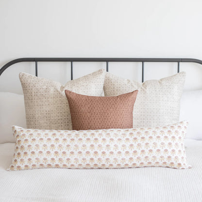 White lumbar pillow with small tan floral pattern, displayed among coordinating neutral and patterned pillows on a bed.