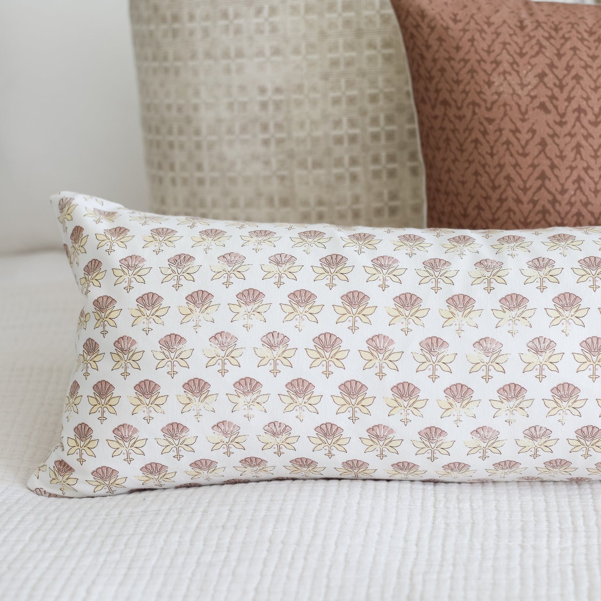 White lumbar pillow with repeating pink and tan floral fan pattern.