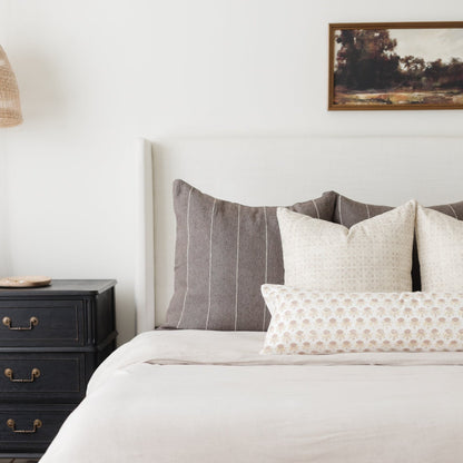 Beige and cream patterned throw pillow displayed on a bed with striped and textured pillows.