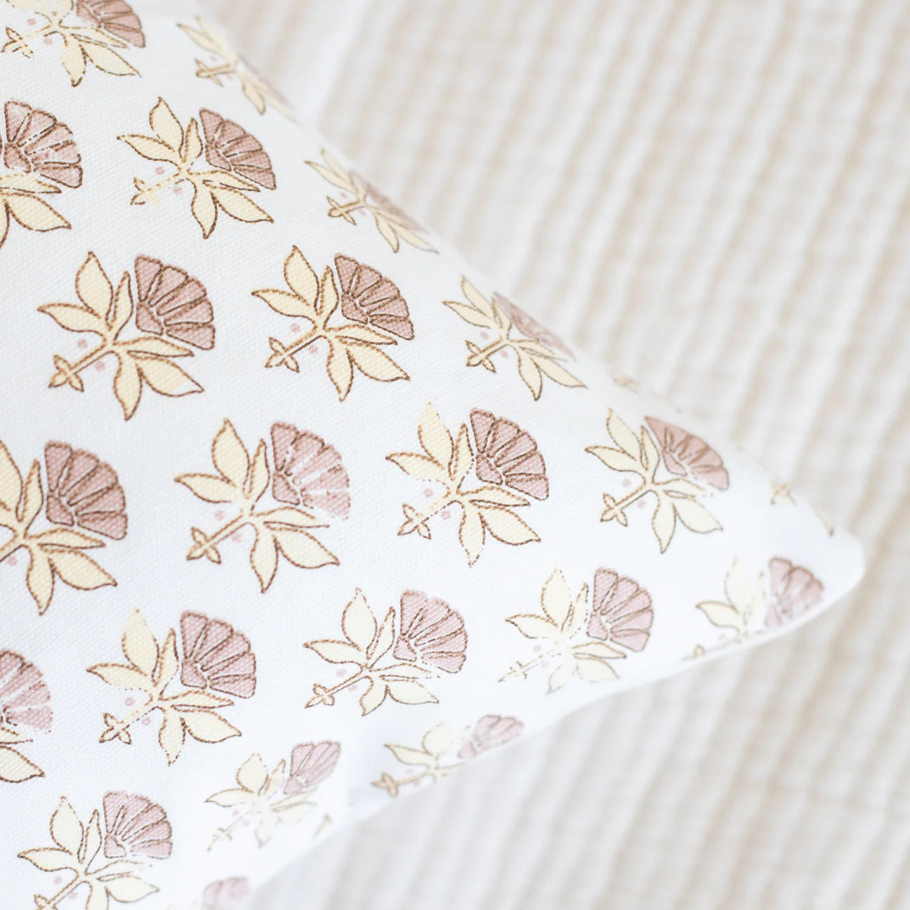 White lumbar pillow with tan and mauve outlined floral pattern, displayed on striped bedding.