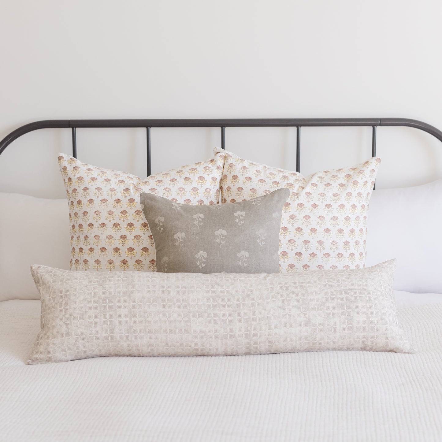 Rectangular lumbar pillow with neutral grid texture displayed on bed with patterned pillows.
