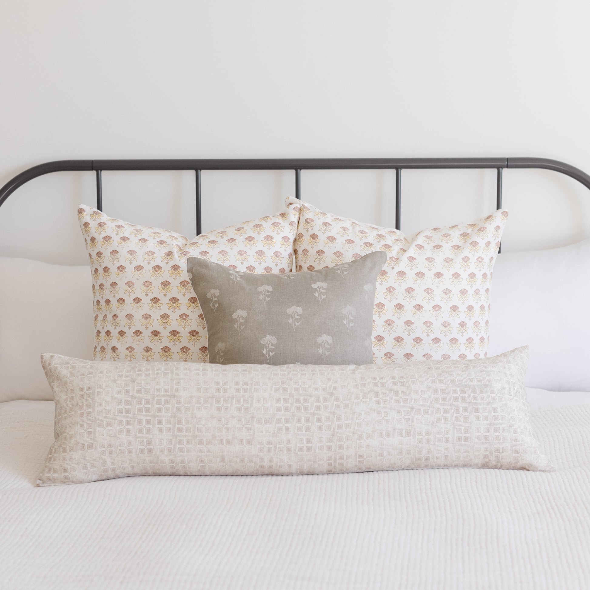 Rectangular lumbar pillow with neutral grid texture displayed on bed with patterned pillows.