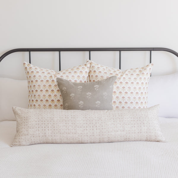 Rectangular lumbar pillow with neutral grid texture displayed on bed with patterned pillows.
