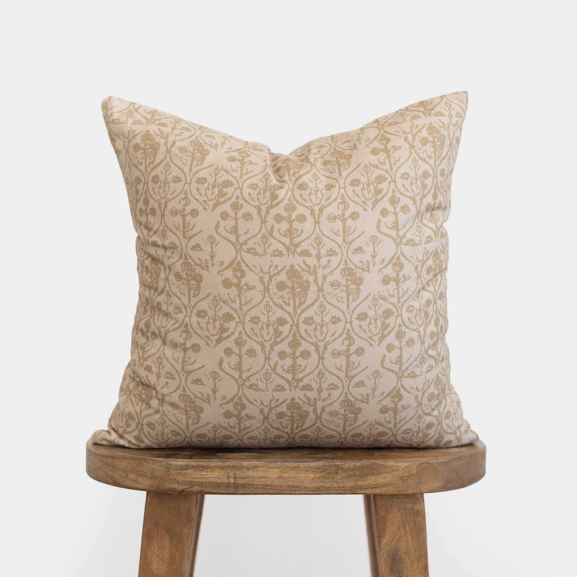 Beige pillow cover with tan floral and geometric pattern, displayed on wooden stool.