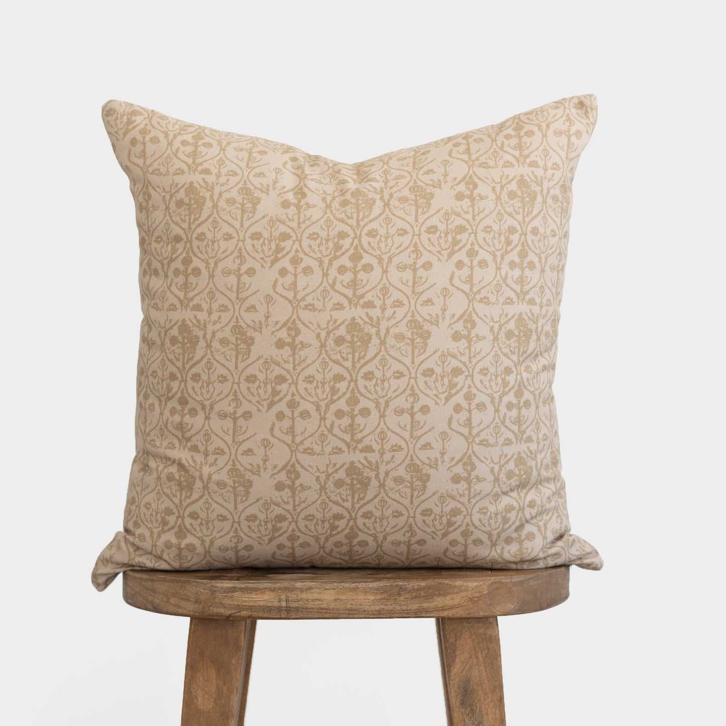 Cream and tan pillow cover with repeating damask floral pattern, displayed on wooden stool.