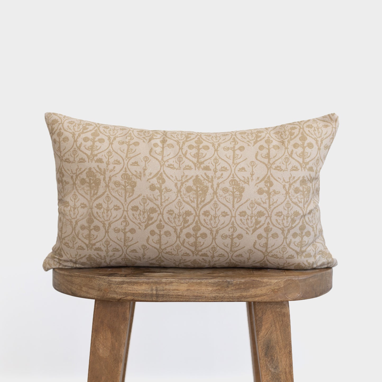 Rectangular pillow with geometric floral pattern in tan and cream on wooden stool.