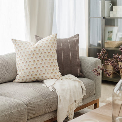 White pillow with tan floral pattern on gray upholstered sofa.