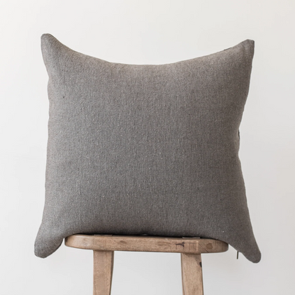 Gray woven pillow with pointed corners resting on a wooden stool.