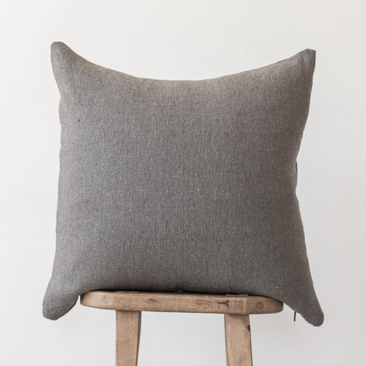 Gray woven pillow with pointed corners resting on a wooden stool.