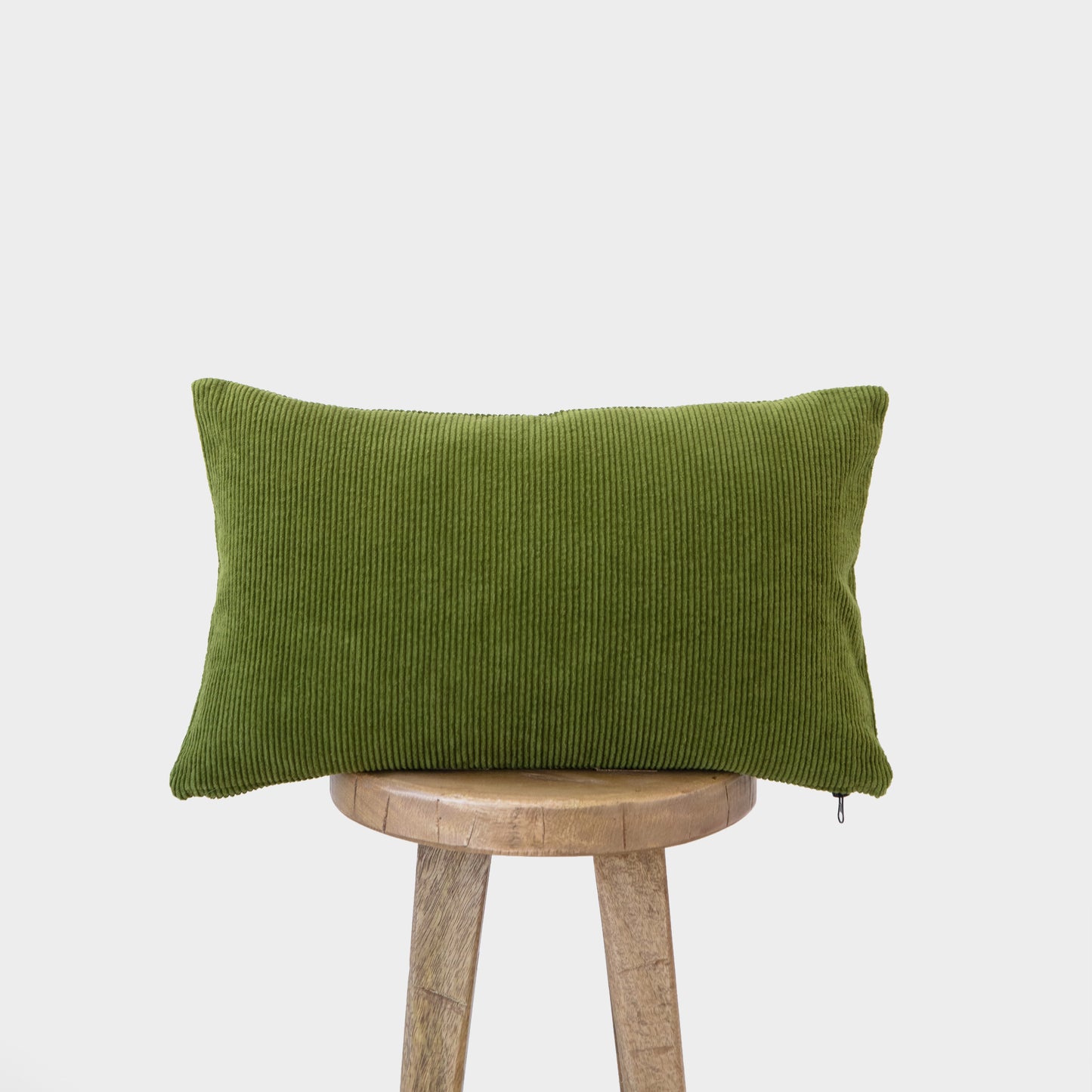 Green corduroy lumbar pillow with vertical ribbed texture displayed on wooden stool.