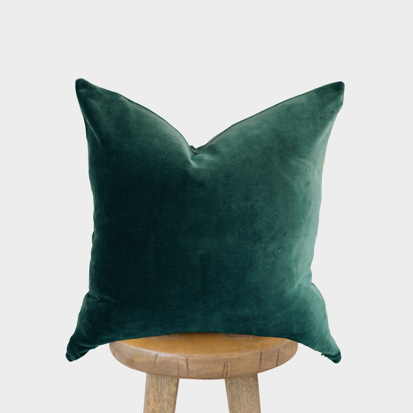 Green velvet throw pillow with pointed corners displayed on a wooden stool.
