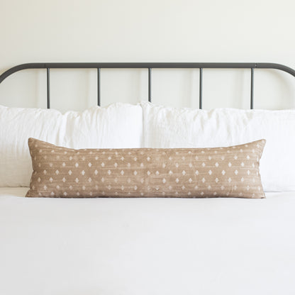 Tan lumbar pillow with white dot pattern on bed with metal headboard and white bedding.
