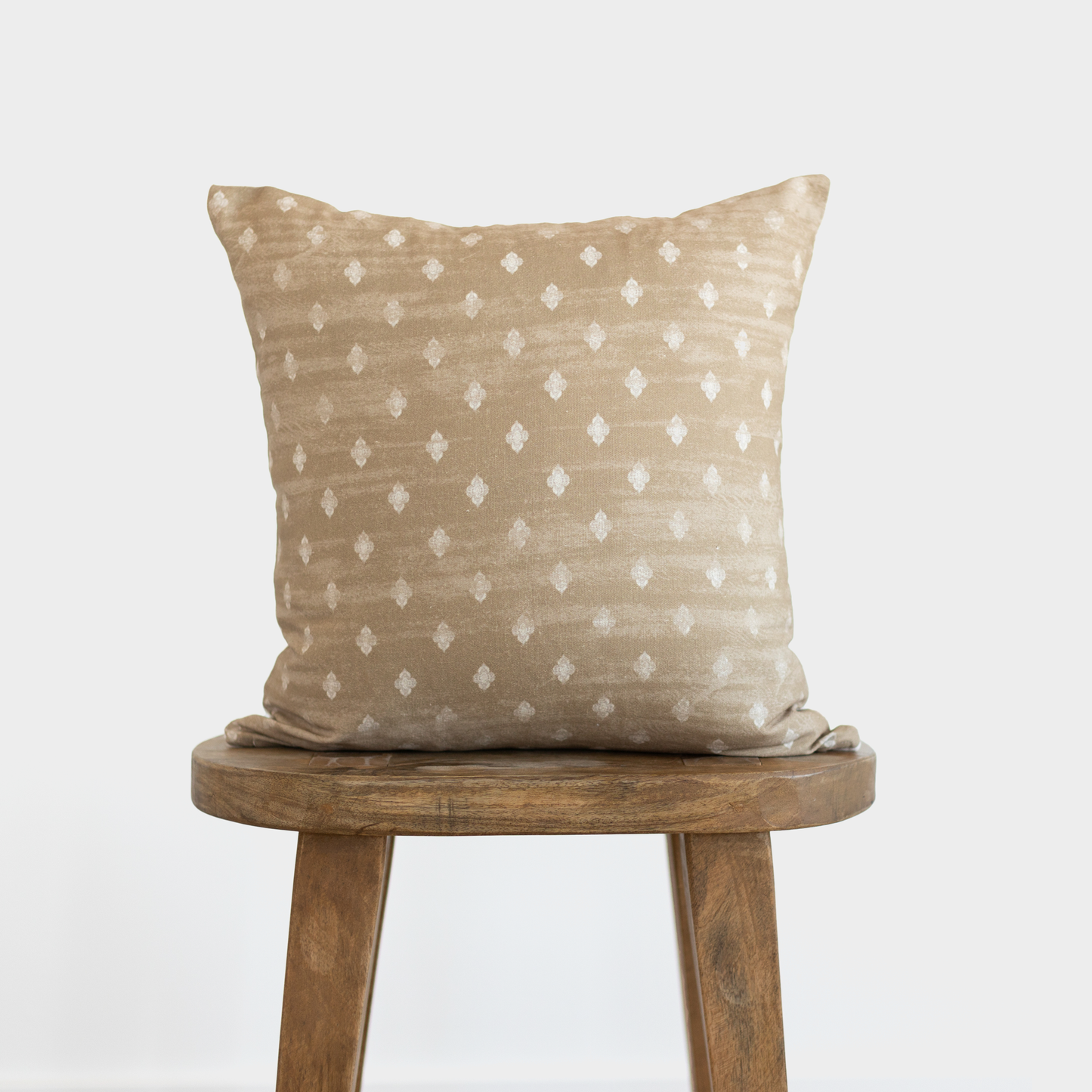 Tan pillow with white diamond pattern displayed on a wooden round stool.