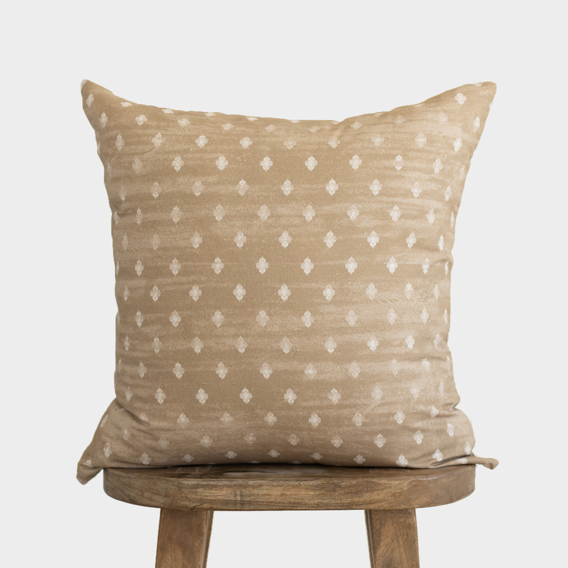 Tan linen pillow with white diamond pattern displayed on wooden stool.