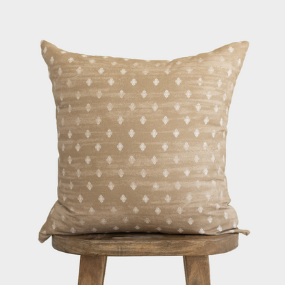 Tan linen pillow with white diamond pattern displayed on wooden stool.
