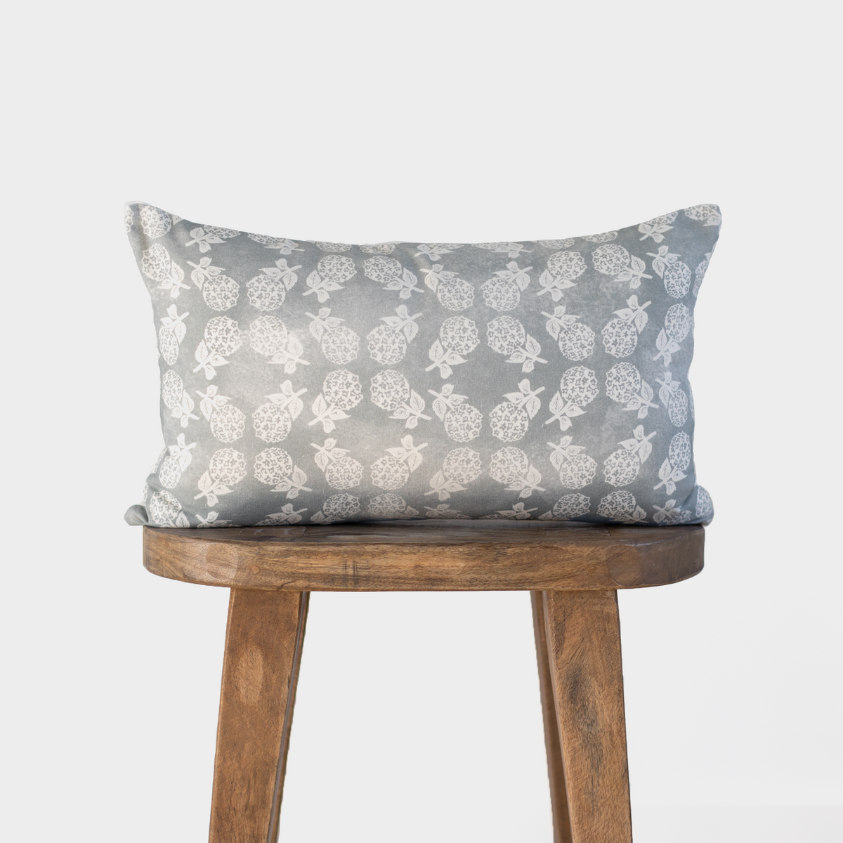 Gray and cream floral patterned pillow with leaf motifs on wooden stool.