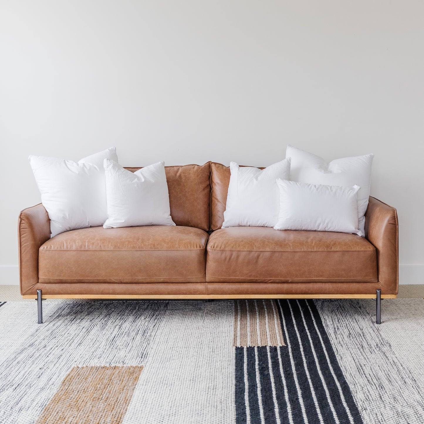 Tan leather sofa with white and brown square cushion inserts arranged across the back.