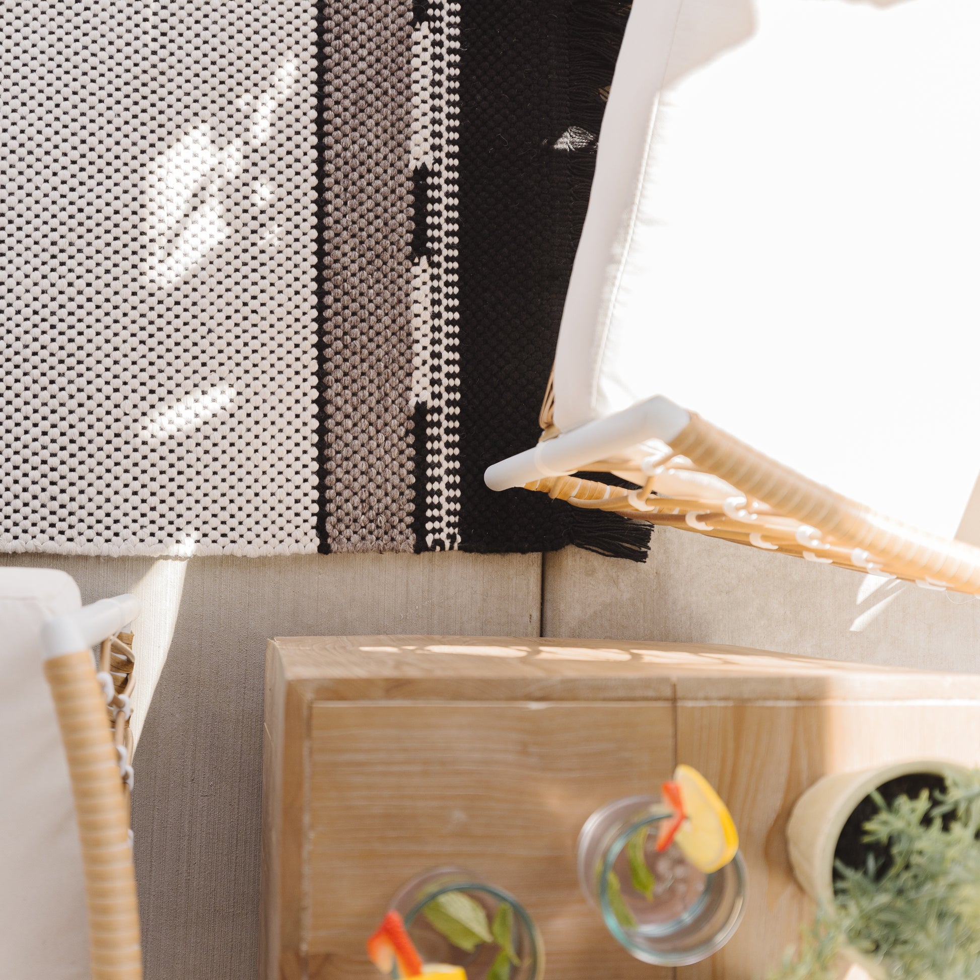 Striped outdoor rug in cream, gray, and black with woven texture displayed on neutral furniture.