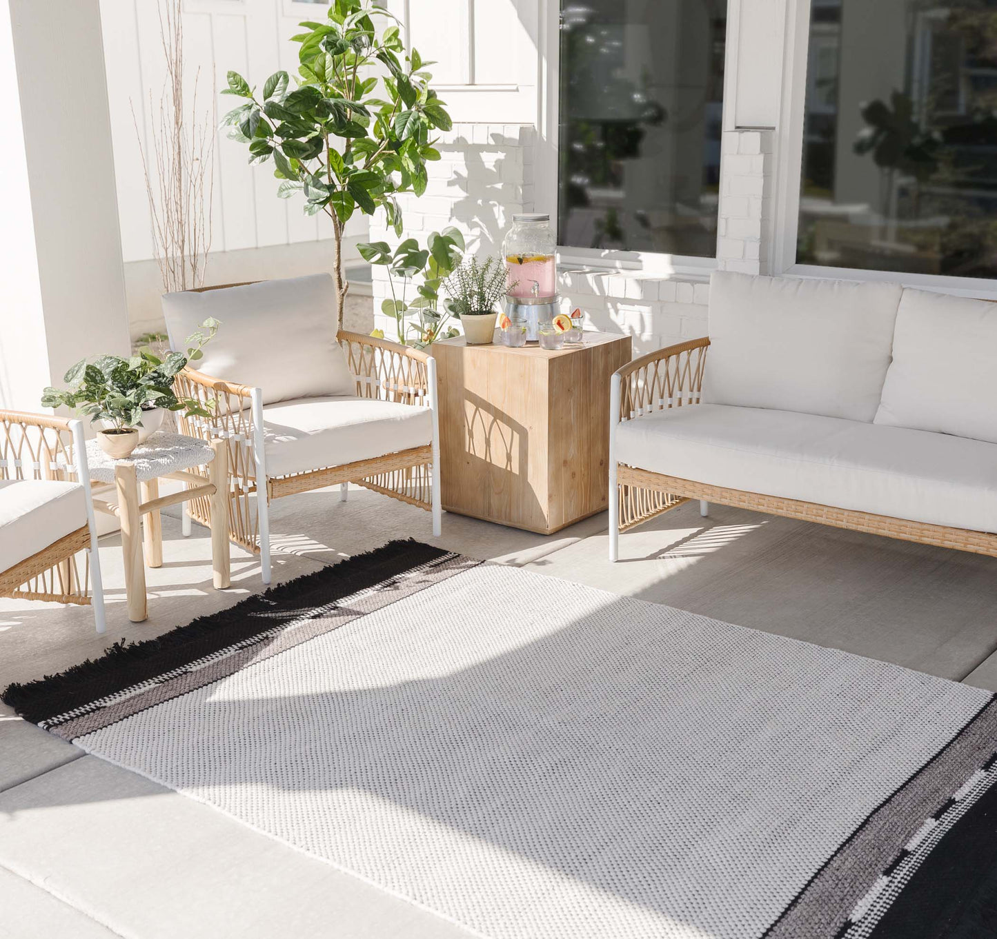 Light gray and white striped outdoor rug on patio with wicker furniture and potted plants.