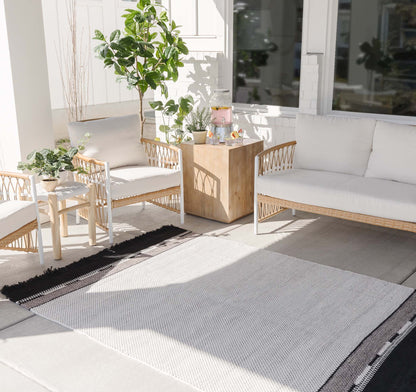 Light gray and white striped outdoor rug on patio with wicker furniture and potted plants.